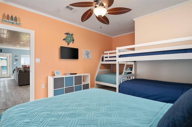 bedroom featuring a ceiling fan, wood finished floors, visible vents, and ornamental molding