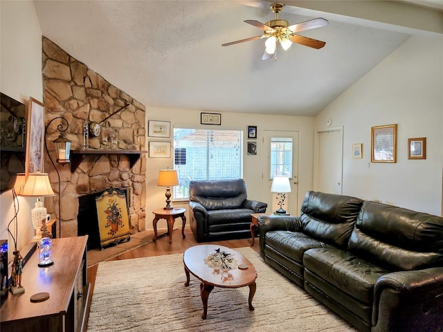 living room with a textured ceiling, wood finished floors, a stone fireplace, lofted ceiling, and ceiling fan