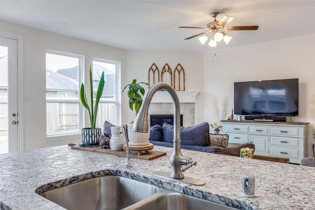 kitchen featuring open floor plan, light stone counters, a fireplace, white cabinets, and a sink