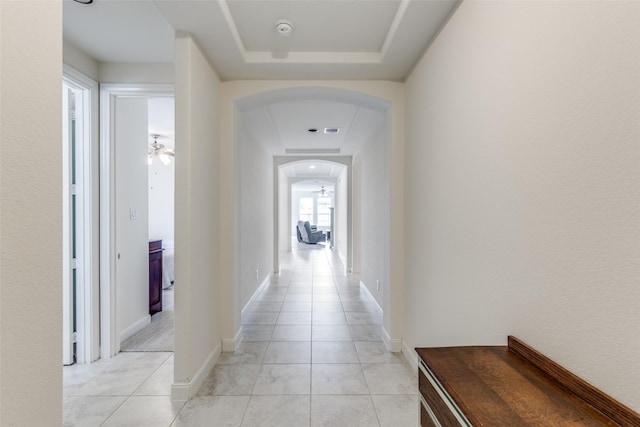 corridor featuring baseboards, arched walkways, a raised ceiling, and visible vents