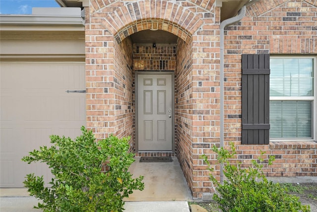 entrance to property featuring an attached garage and brick siding