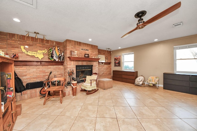 living area with a ceiling fan, brick wall, tile patterned flooring, a textured ceiling, and a brick fireplace