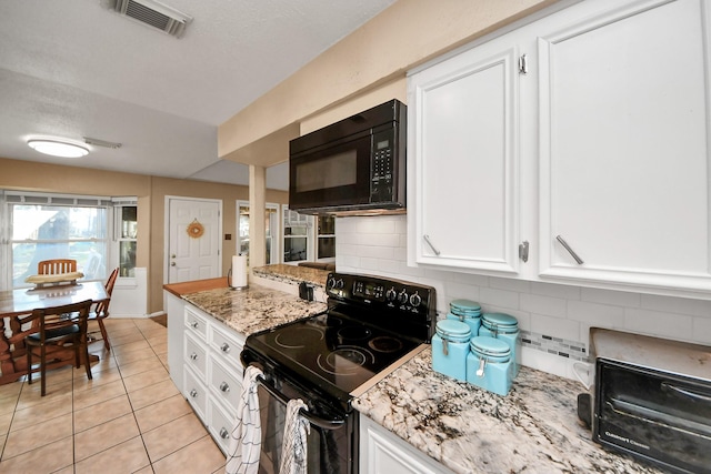 kitchen with light tile patterned floors, white cabinets, black appliances, and light stone countertops