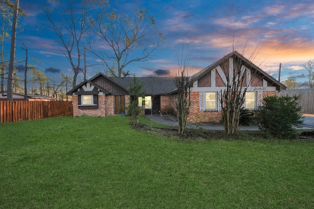 rear view of house featuring brick siding, a lawn, and fence