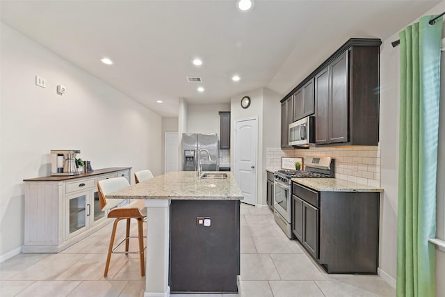 kitchen with an island with sink, a kitchen breakfast bar, tasteful backsplash, appliances with stainless steel finishes, and light tile patterned floors