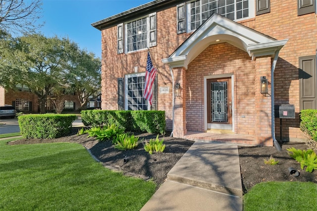 doorway to property featuring brick siding and a lawn