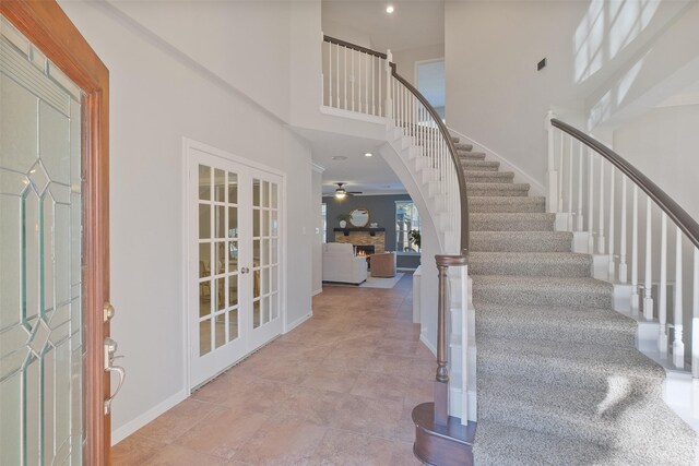 entrance foyer with baseboards, stairs, a lit fireplace, french doors, and a high ceiling