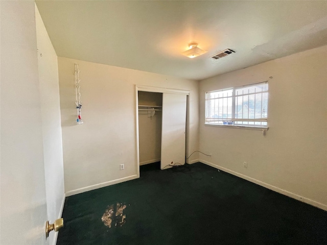 unfurnished bedroom with dark carpet, baseboards, visible vents, and a closet