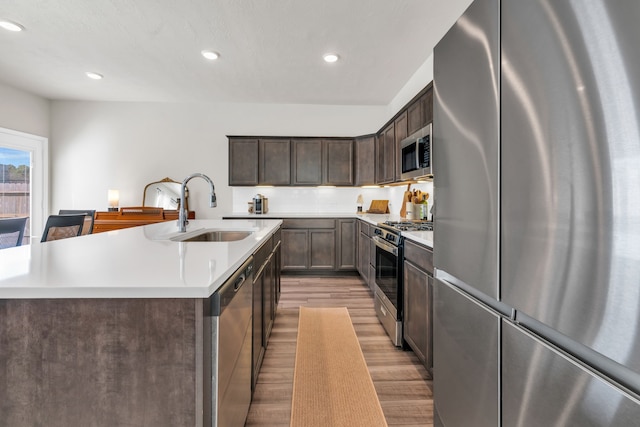 kitchen featuring light wood finished floors, dark brown cabinetry, light countertops, appliances with stainless steel finishes, and a sink