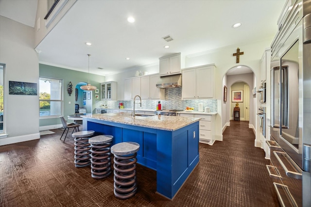 kitchen with arched walkways, a sink, under cabinet range hood, appliances with stainless steel finishes, and a kitchen bar