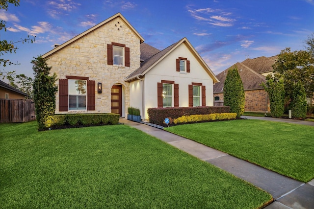 view of front of house with stucco siding, stone siding, a front yard, and fence