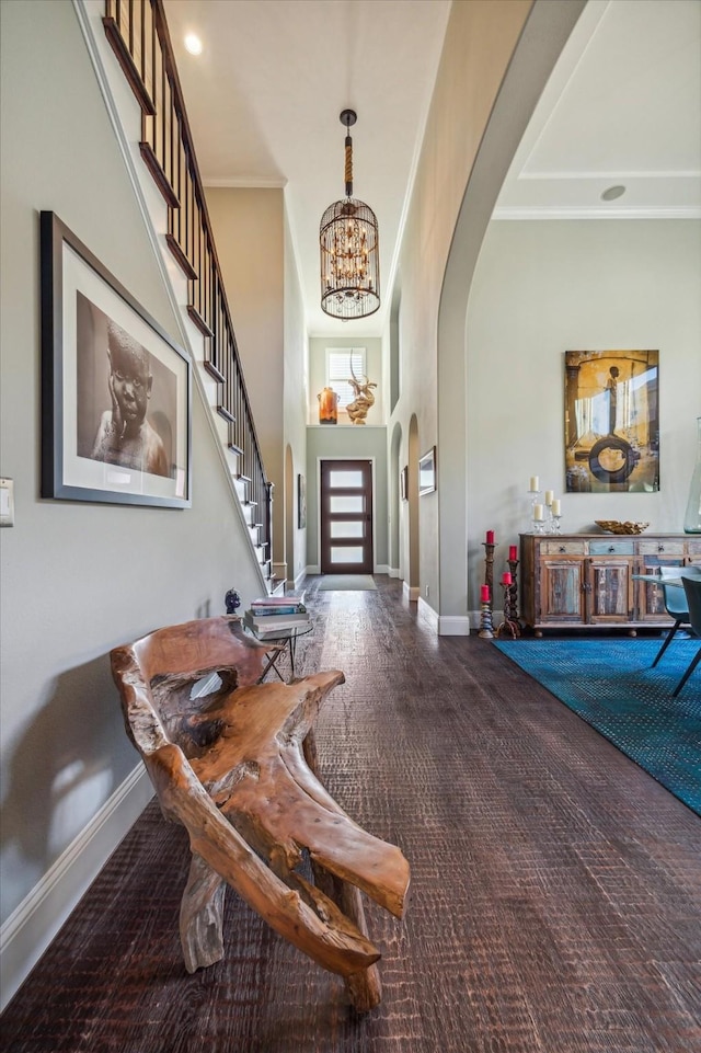 entrance foyer featuring baseboards, a high ceiling, arched walkways, ornamental molding, and stairs