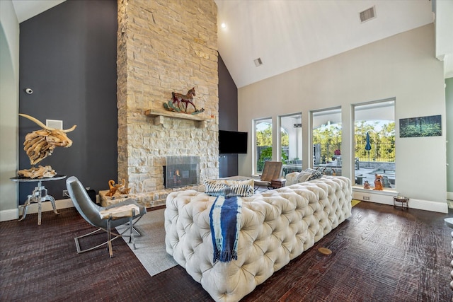 living area with visible vents, high vaulted ceiling, wood finished floors, a stone fireplace, and baseboards