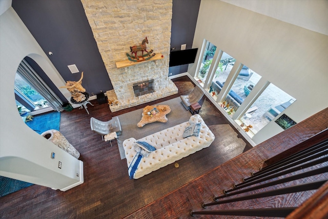 living area with a high ceiling, a stone fireplace, and wood finished floors