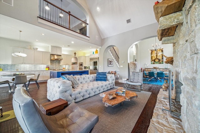 living area featuring visible vents, wood finished floors, arched walkways, an inviting chandelier, and a towering ceiling