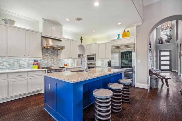 kitchen featuring crown molding, under cabinet range hood, arched walkways, stainless steel appliances, and a sink