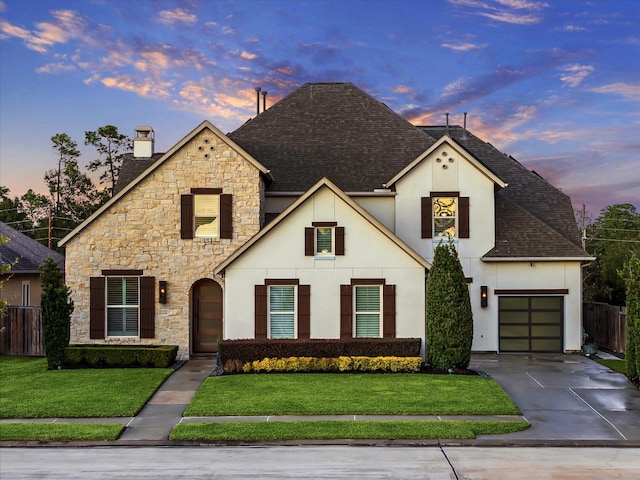 french country inspired facade with a yard, roof with shingles, concrete driveway, and an attached garage