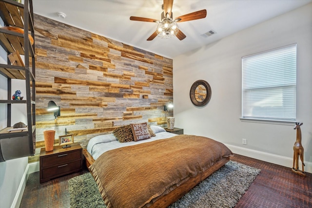 bedroom featuring an accent wall, baseboards, visible vents, and wood walls