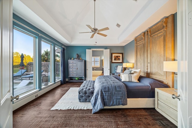 bedroom with visible vents, ensuite bathroom, a tray ceiling, wood finished floors, and access to exterior