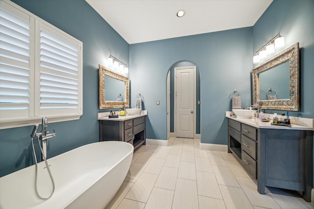 bathroom featuring baseboards, two vanities, recessed lighting, a freestanding tub, and a sink