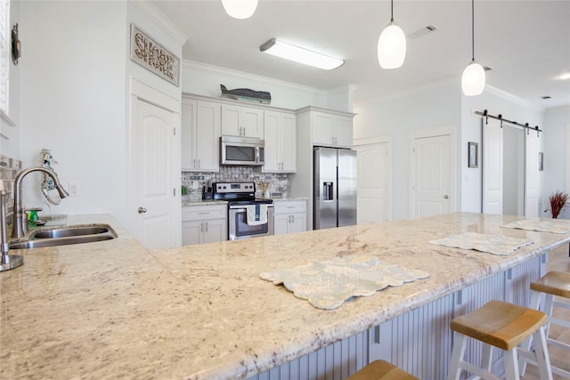 kitchen with a barn door, ornamental molding, a kitchen breakfast bar, stainless steel appliances, and a sink