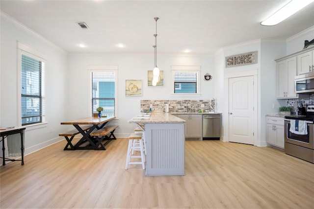 kitchen featuring light wood finished floors, appliances with stainless steel finishes, a breakfast bar, and a peninsula