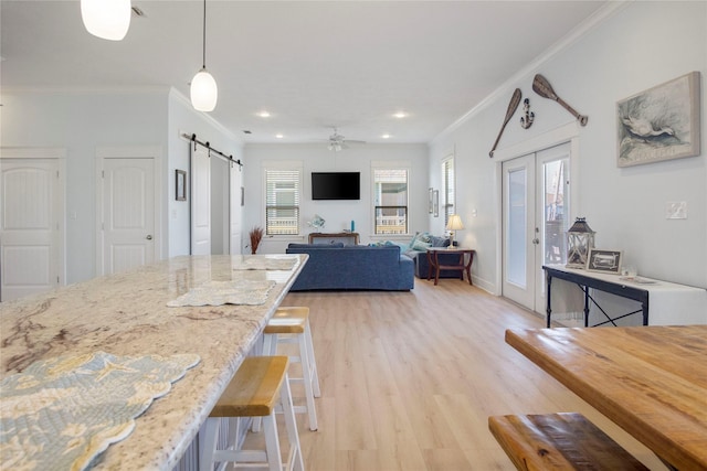 kitchen featuring light wood-style flooring, a kitchen bar, a barn door, and ornamental molding