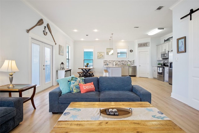 living area featuring visible vents, a barn door, french doors, crown molding, and light wood finished floors