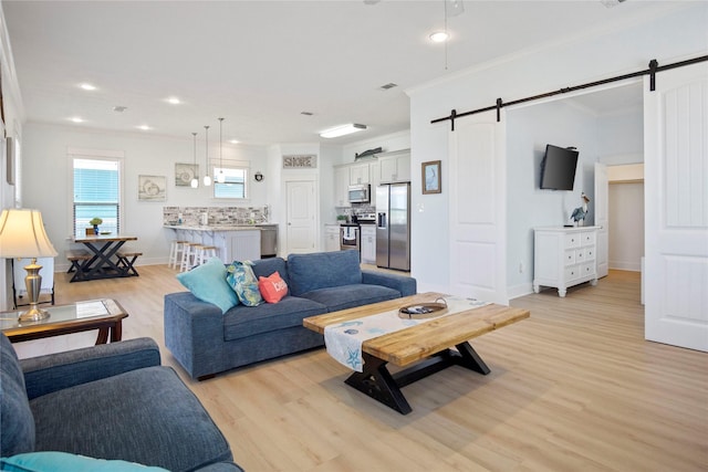 living room with light wood finished floors, baseboards, crown molding, and a barn door