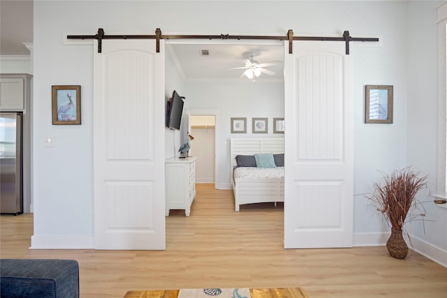 bedroom featuring a barn door, stainless steel fridge, ornamental molding, and light wood-style flooring