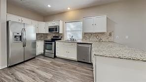 kitchen featuring backsplash, appliances with stainless steel finishes, wood finished floors, white cabinets, and a sink