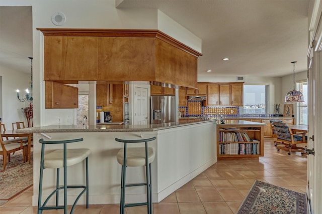 kitchen with brown cabinetry, light tile patterned floors, stainless steel fridge with ice dispenser, and a peninsula