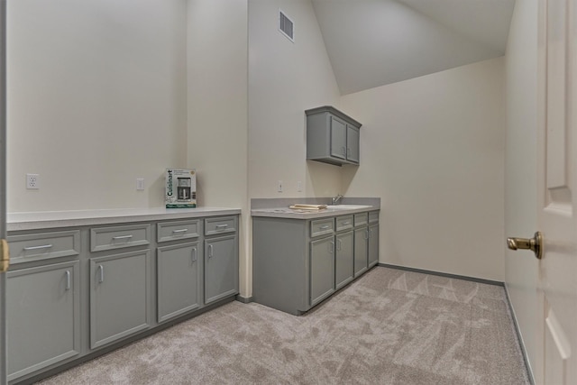 kitchen with visible vents, lofted ceiling, a sink, gray cabinetry, and light colored carpet