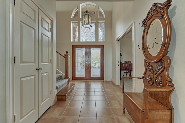 entrance foyer with a chandelier, stairs, light tile patterned floors, french doors, and a towering ceiling