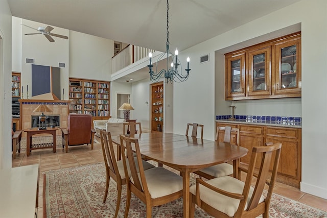 dining area with light tile patterned floors, visible vents, ceiling fan with notable chandelier, and a tile fireplace