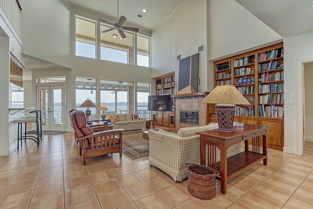 living area with light tile patterned floors, a tiled fireplace, a ceiling fan, and french doors