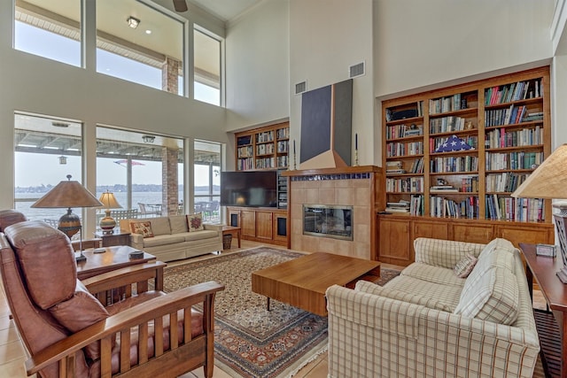 living area with built in features, visible vents, a high ceiling, and a tiled fireplace