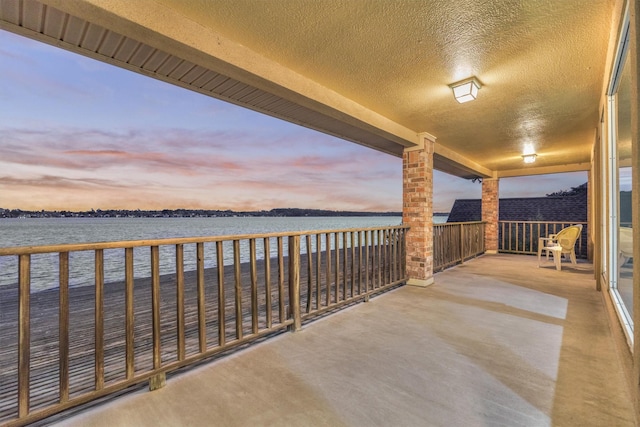 patio terrace at dusk featuring a balcony and a water view