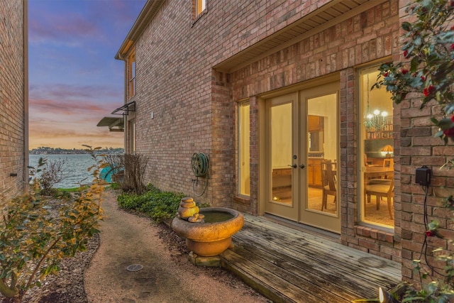 entrance to property featuring french doors, a water view, and brick siding