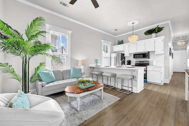 living room with visible vents, a healthy amount of sunlight, crown molding, and wood finished floors