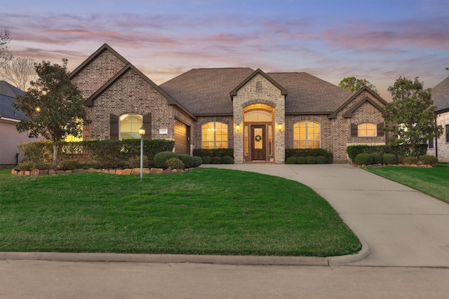 french provincial home featuring a front lawn, brick siding, driveway, and a shingled roof