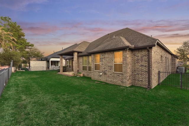 rear view of house with a yard, brick siding, roof with shingles, and a fenced backyard