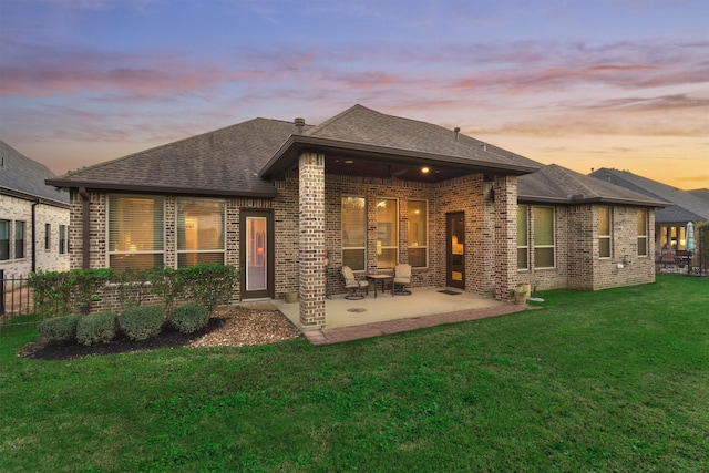 rear view of property featuring a patio, fence, a shingled roof, a lawn, and brick siding