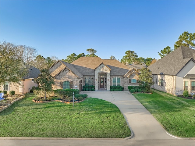 french country home featuring brick siding, stone siding, driveway, and a front yard