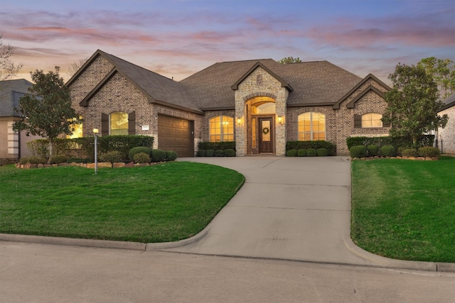 french country home featuring brick siding, a lawn, an attached garage, and concrete driveway