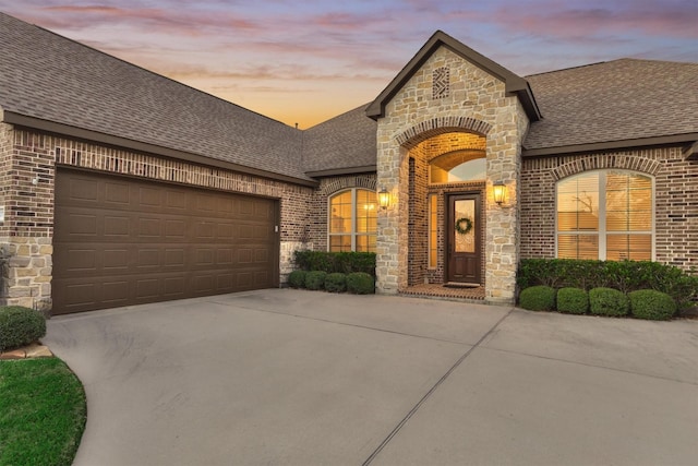 french country style house featuring concrete driveway, brick siding, and roof with shingles