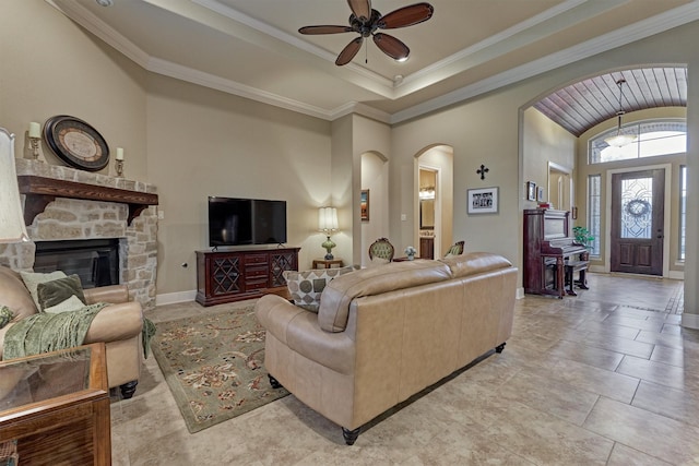 living room with baseboards, a tray ceiling, a fireplace, arched walkways, and ornamental molding