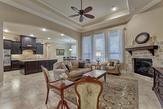 living room featuring a tray ceiling, visible vents, arched walkways, and ornamental molding