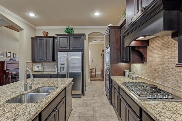 kitchen with premium range hood, a sink, light stone counters, stainless steel appliances, and arched walkways