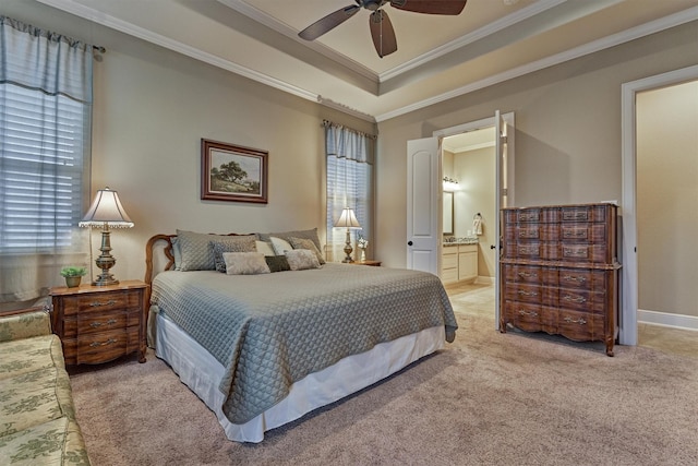 bedroom featuring light carpet, ornamental molding, a tray ceiling, ensuite bath, and ceiling fan